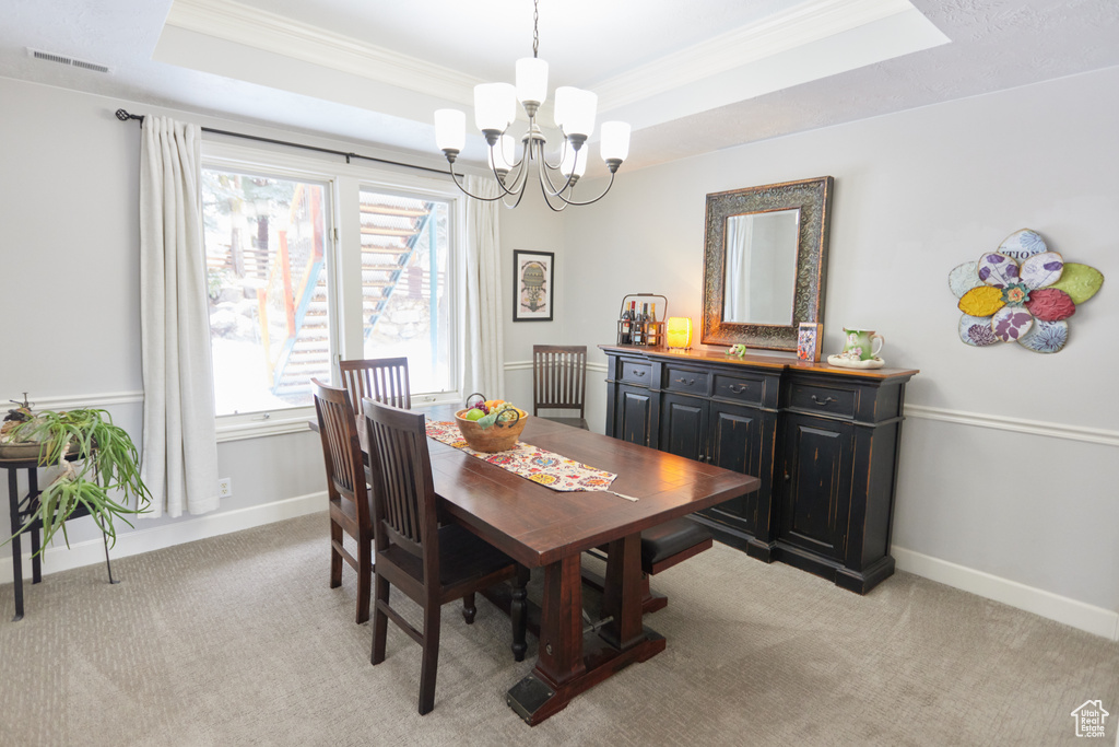 Dining room featuring a chandelier, ornamental molding, a tray ceiling, and light colored carpet