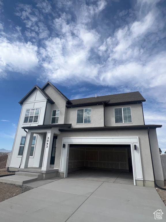 View of front of house with a garage, driveway, and stucco siding