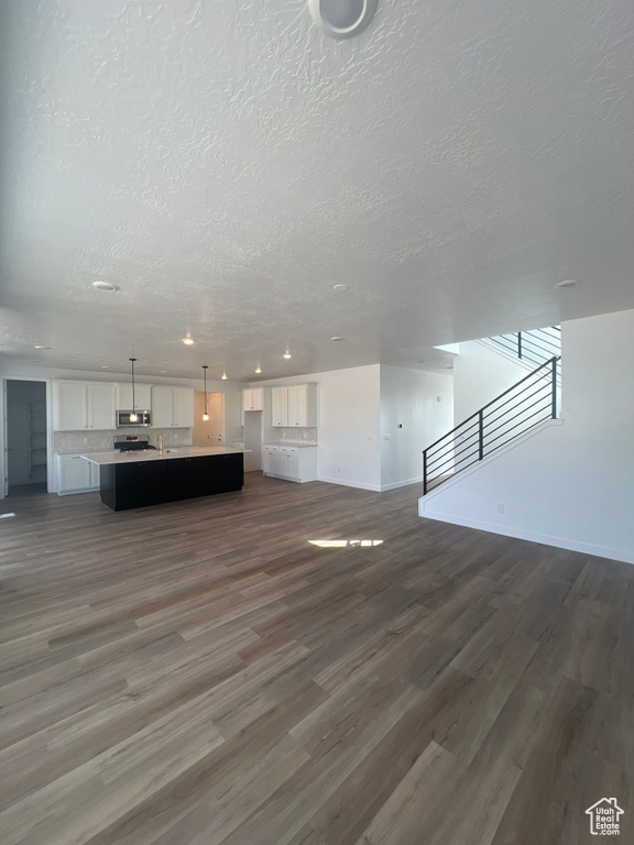 Unfurnished living room with dark wood-style floors, a textured ceiling, stairway, and recessed lighting