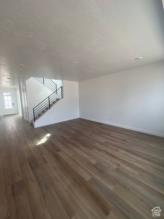 Unfurnished living room featuring a textured ceiling, stairs, and dark wood finished floors