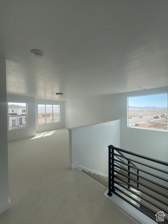 Corridor with an upstairs landing, carpet, and a textured ceiling