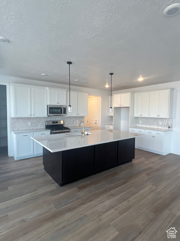 Kitchen with appliances with stainless steel finishes, tasteful backsplash, a textured ceiling, white cabinetry, and a large island