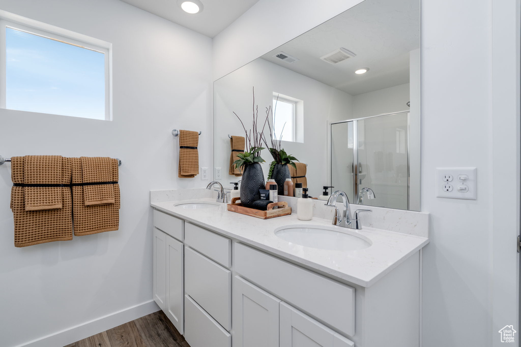 Bathroom featuring double vanity, wood finished floors, and a shower with door