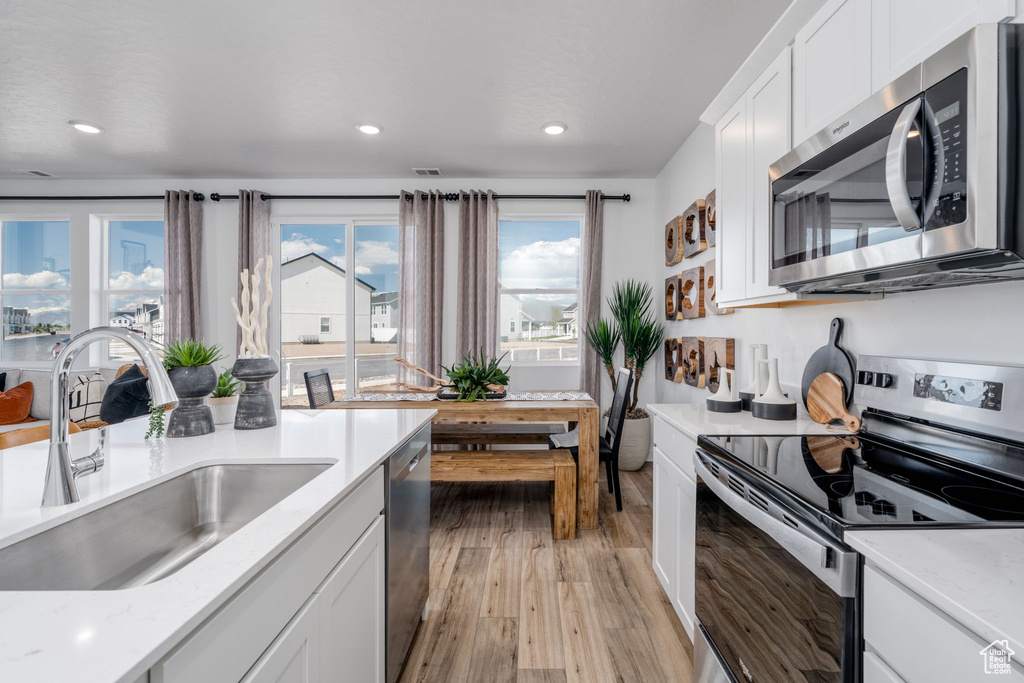 Kitchen featuring stainless steel appliances, light wood-style floors, recessed lighting, white cabinetry, and light stone counters