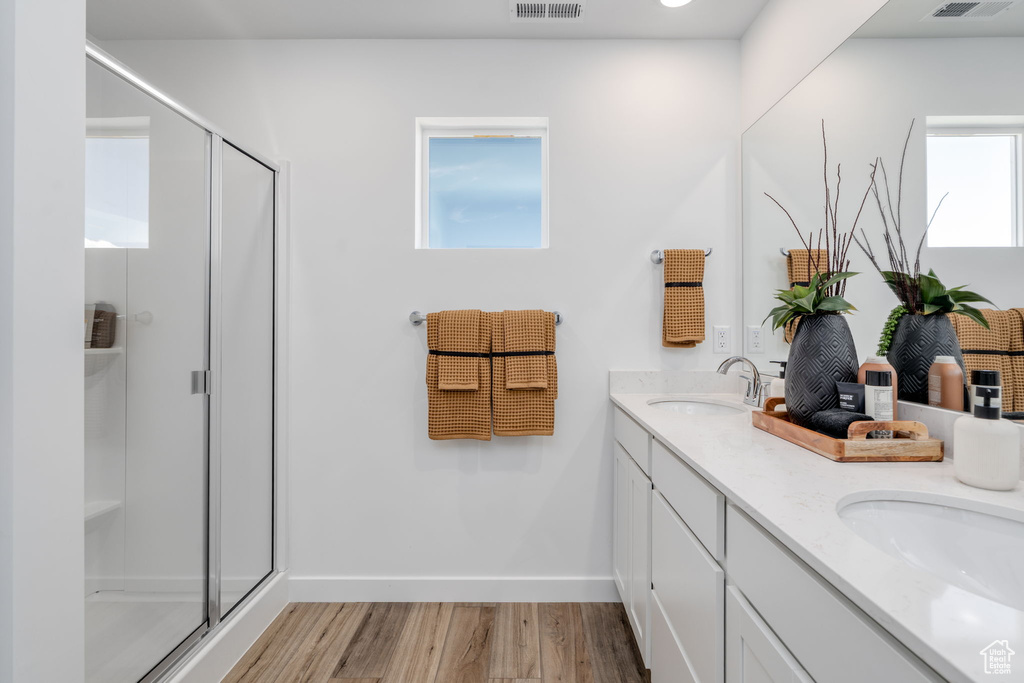 Bathroom featuring wood finished floors, double vanity, and a stall shower