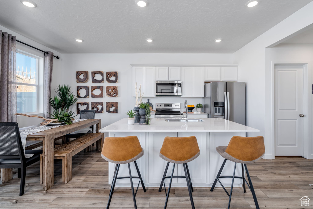 Kitchen featuring stainless steel appliances, a kitchen island with sink, a breakfast bar area, light countertops, and recessed lighting