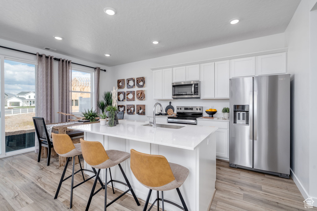 Kitchen with stainless steel appliances, a kitchen island with sink, a breakfast bar, white cabinets, and light wood-style floors