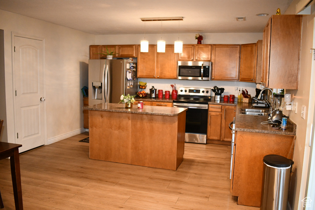 Kitchen with appliances with stainless steel finishes, a center island, light wood-style flooring, and brown cabinetry