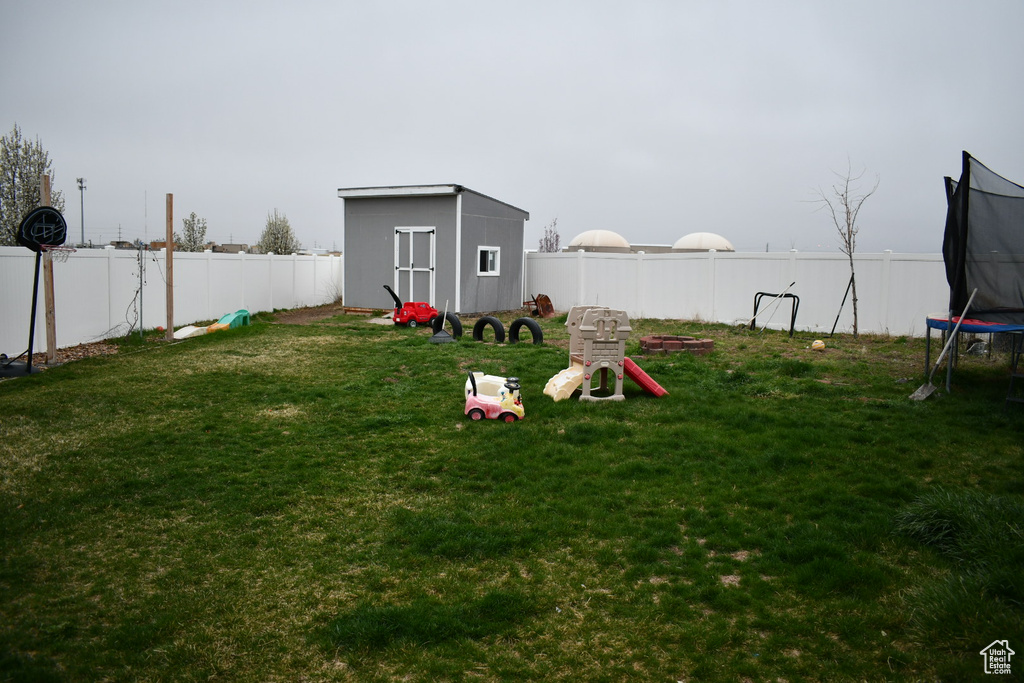 Fenced backyard featuring a trampoline and a storage shed
