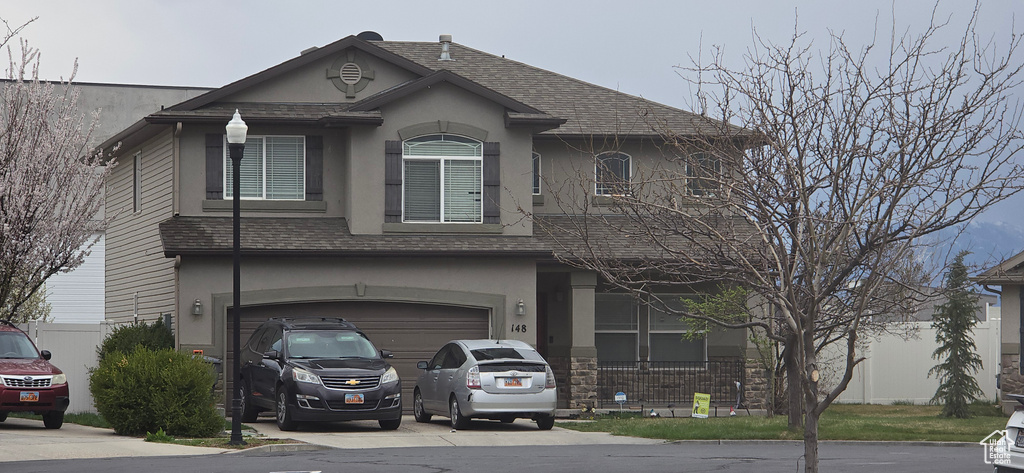 View of front of home with stucco siding, driveway, a garage, and roof with shingles
