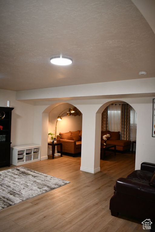 Living area featuring arched walkways, light wood-style floors, and a textured ceiling