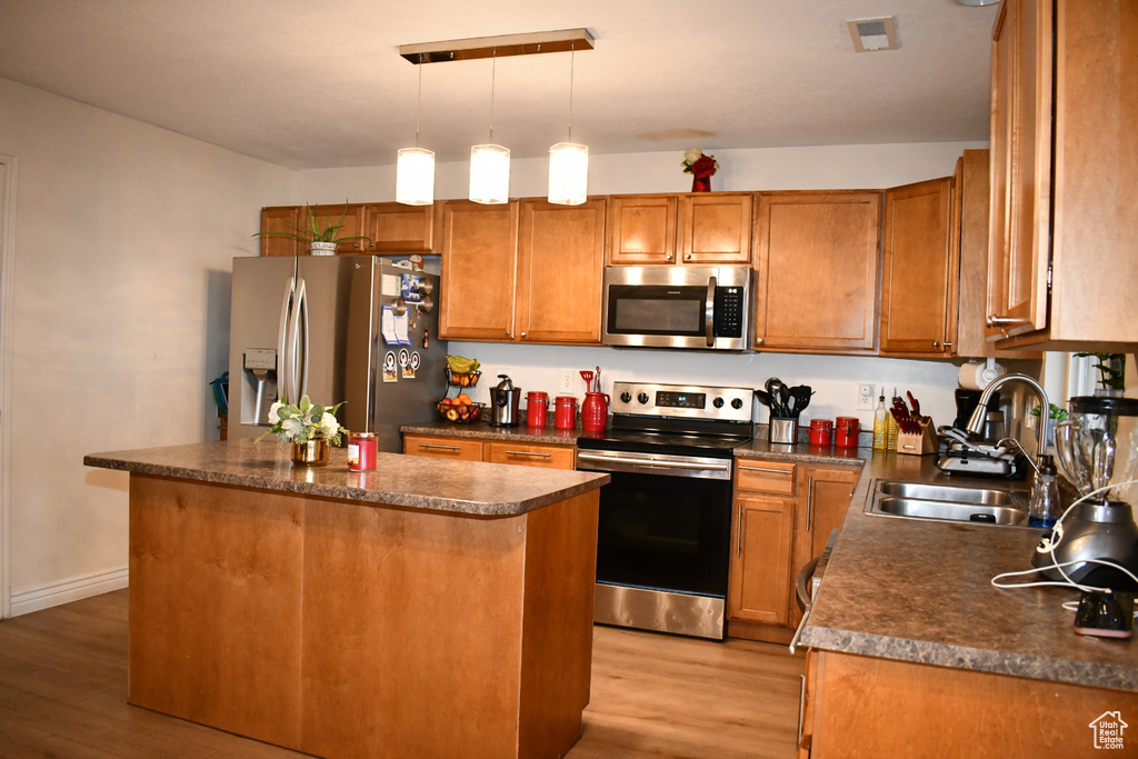Kitchen with stainless steel appliances, light wood finished floors, dark countertops, a center island, and brown cabinetry
