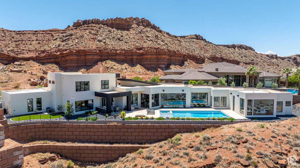 Back of property featuring stucco siding, a patio area, an outdoor pool, and a mountain view