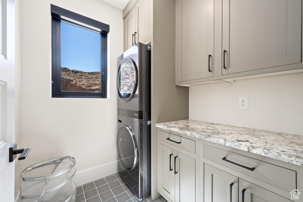 Washroom with stacked washer and clothes dryer, cabinet space, and dark tile patterned flooring