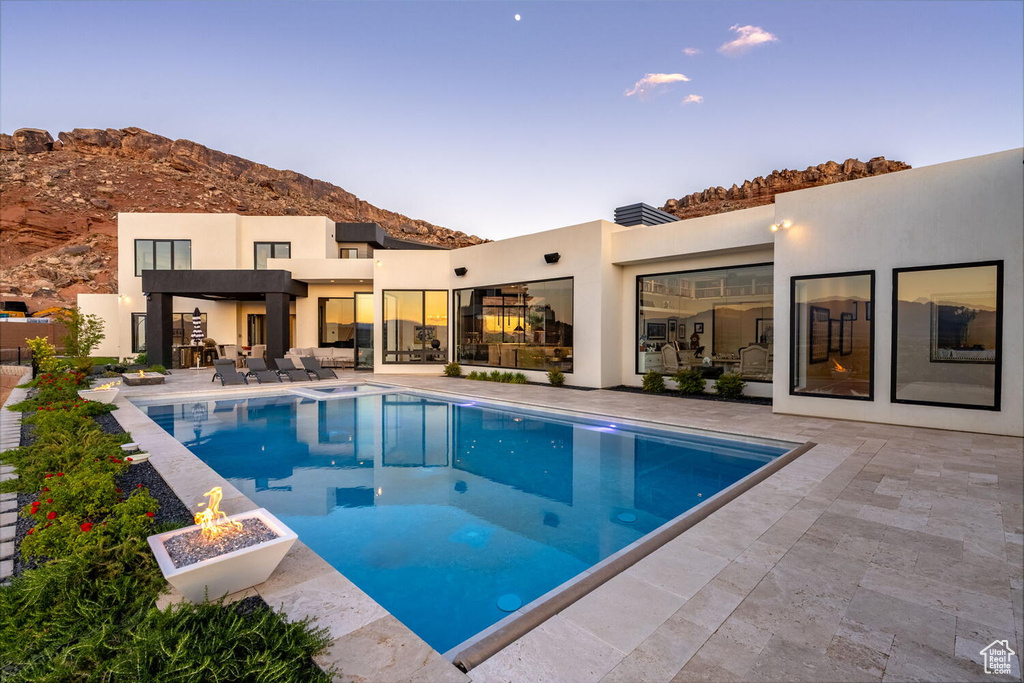 Pool at dusk with an outdoor pool, an outdoor fire pit, a patio, and a mountain view