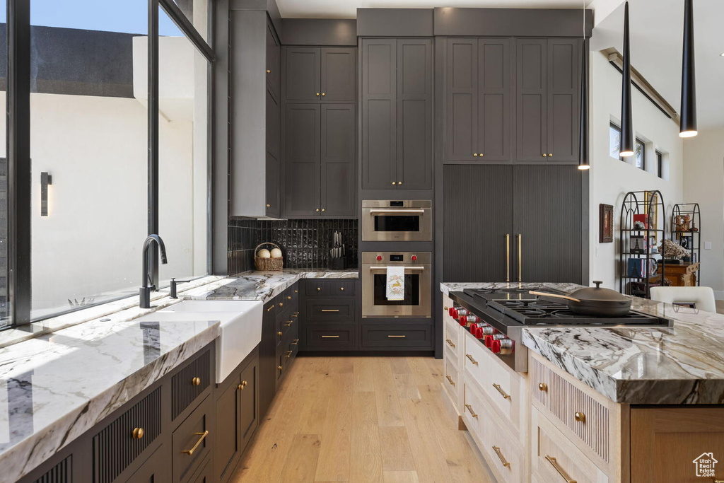 Kitchen featuring stainless steel appliances, light wood finished floors, light stone counters, and decorative backsplash