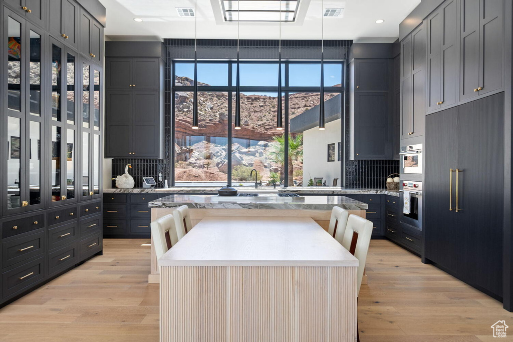 Kitchen with light wood finished floors, recessed lighting, a kitchen island, light stone countertops, and double oven
