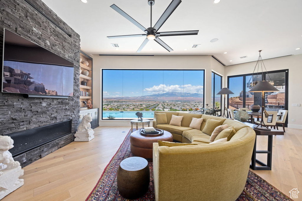 Living room featuring hardwood / wood-style flooring, a stone fireplace, built in shelves, ceiling fan, and recessed lighting