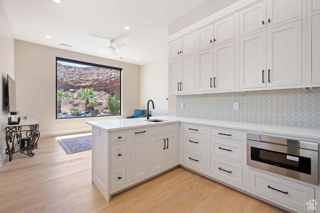 Kitchen featuring a peninsula, light wood-type flooring, backsplash, a ceiling fan, and light countertops