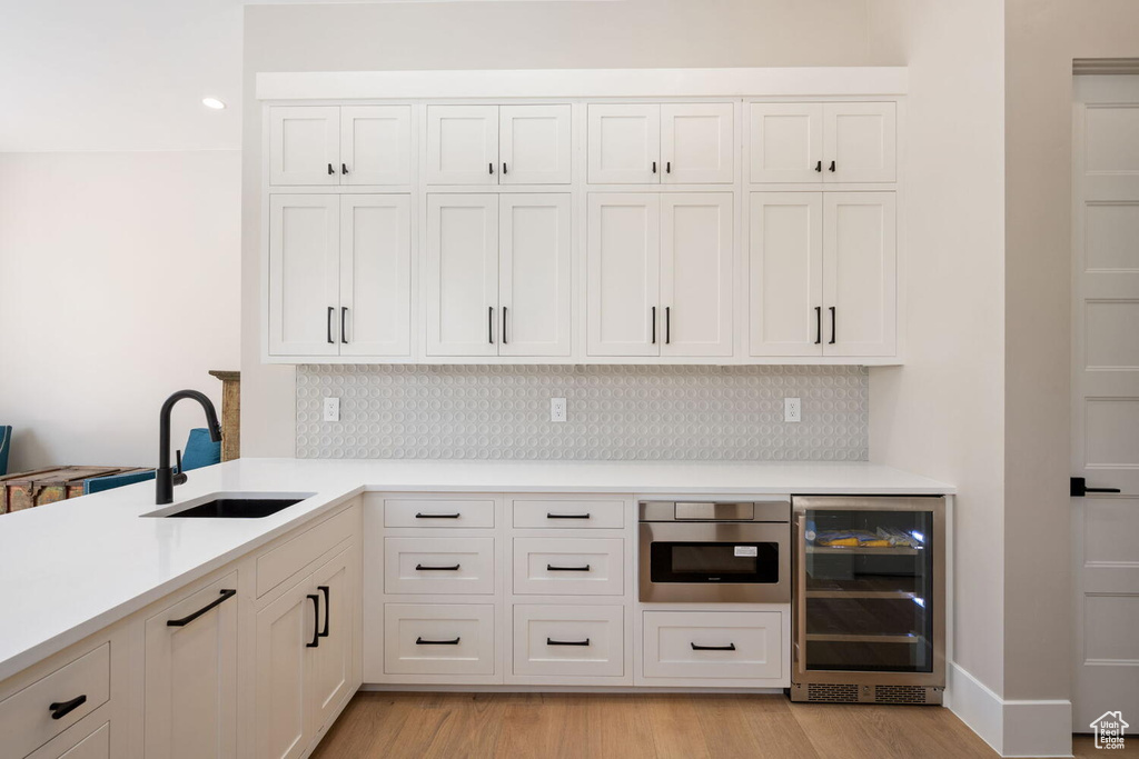 Kitchen featuring wine cooler, backsplash, light countertops, light wood-style flooring, and white cabinetry