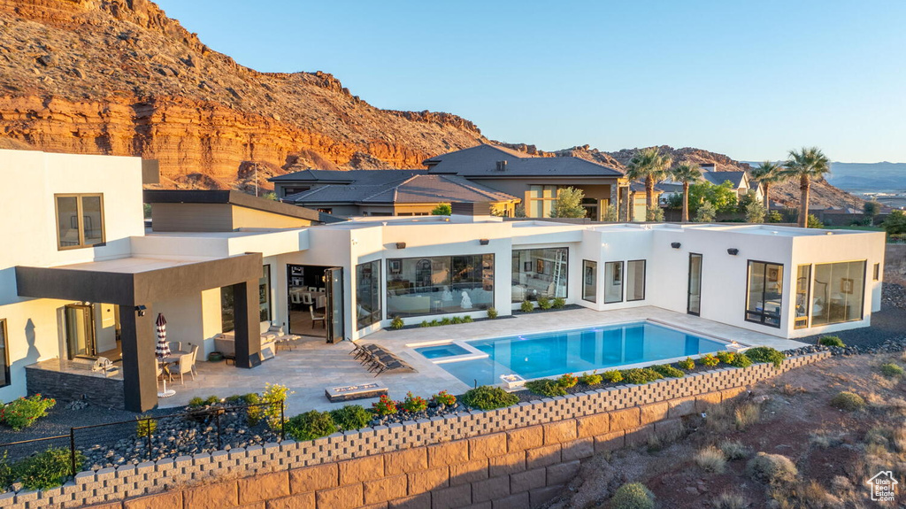 Rear view of house featuring stucco siding, a mountain view, a patio area, and a pool with connected hot tub