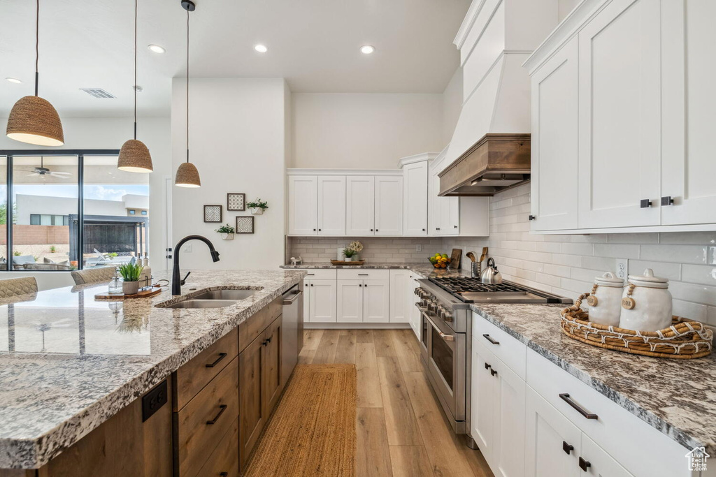 Kitchen featuring stainless steel appliances, custom range hood, light wood-style flooring, white cabinetry, and recessed lighting