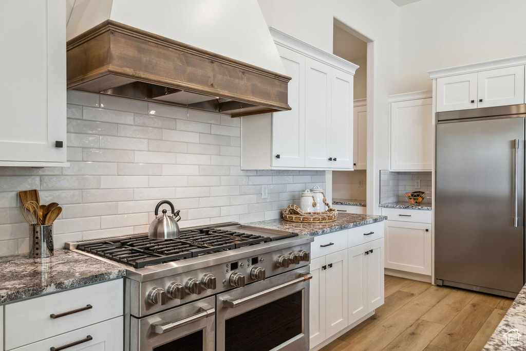 Kitchen with high quality appliances, custom exhaust hood, white cabinetry, backsplash, and stone counters