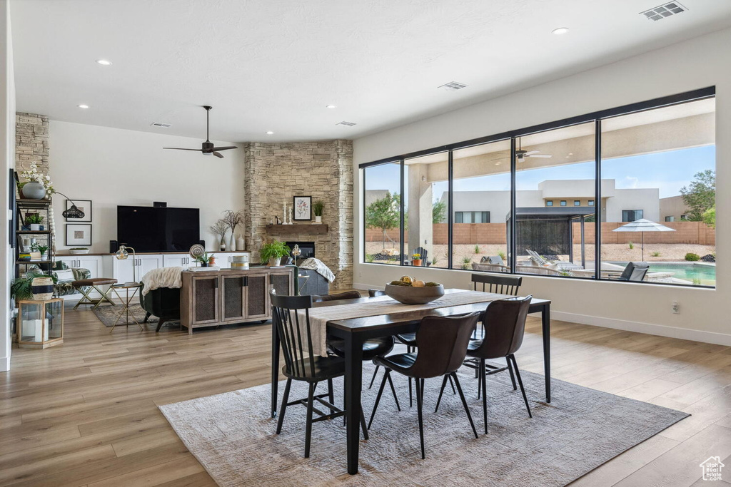 Dining area with a ceiling fan, a stone fireplace, light wood-type flooring, and recessed lighting