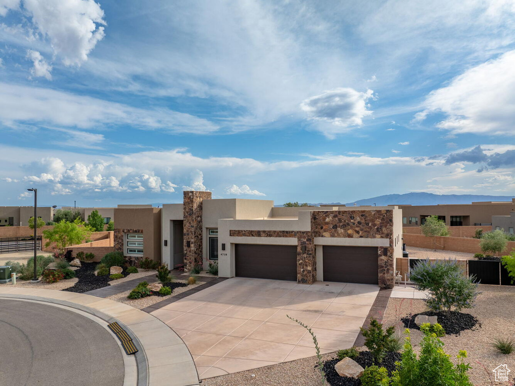 Adobe home featuring an attached garage, concrete driveway, stucco siding, and stone siding