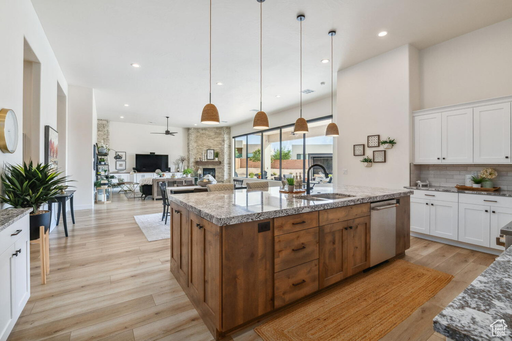 Kitchen with a fireplace, dishwasher, a center island with sink, a ceiling fan, and backsplash