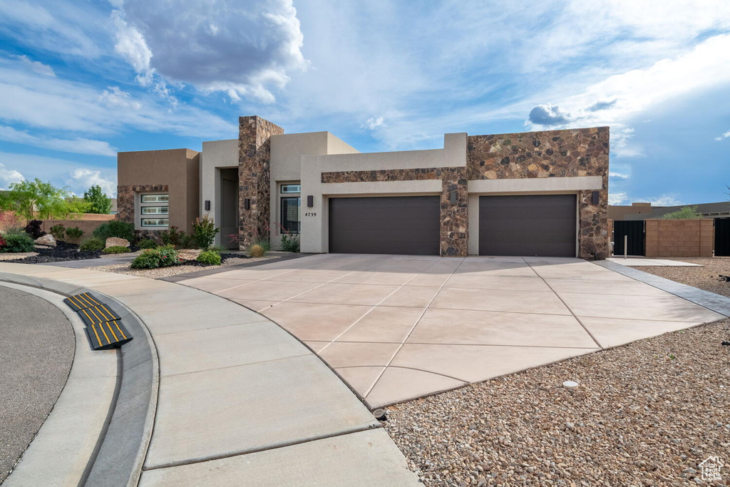 View of front of home with a garage, concrete driveway, stucco siding, and stone siding