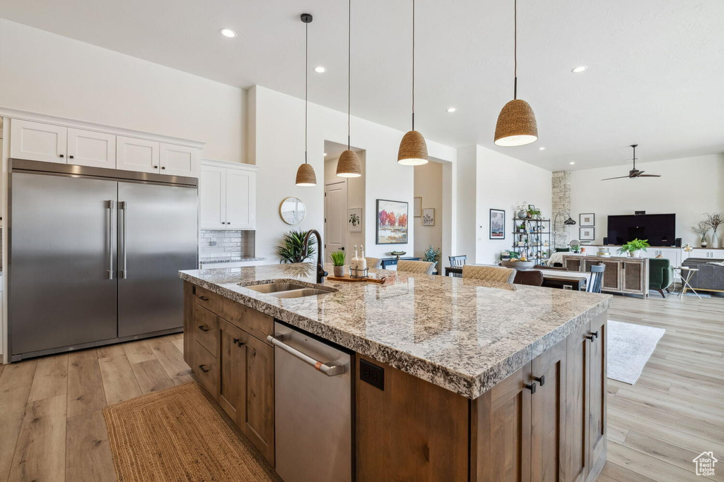 Kitchen featuring stainless steel appliances, a ceiling fan, light wood finished floors, an island with sink, and white cabinetry