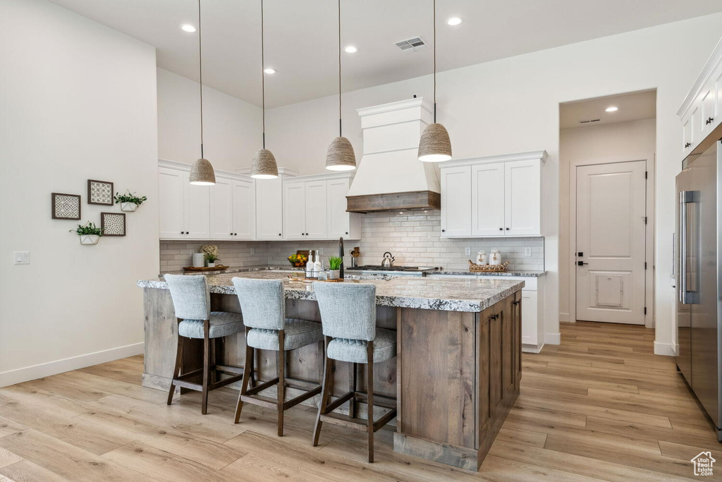 Kitchen featuring wall chimney exhaust hood, white cabinetry, a kitchen island with sink, recessed lighting, and a high ceiling