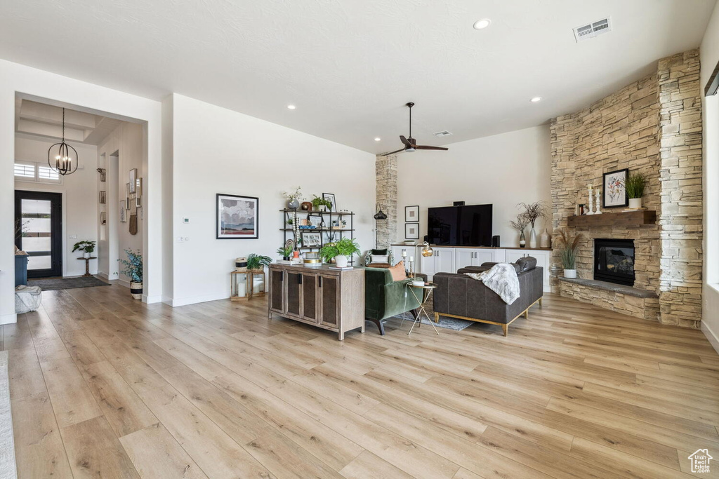 Living area with light wood-style floors, ceiling fan, a chandelier, recessed lighting, and a stone fireplace
