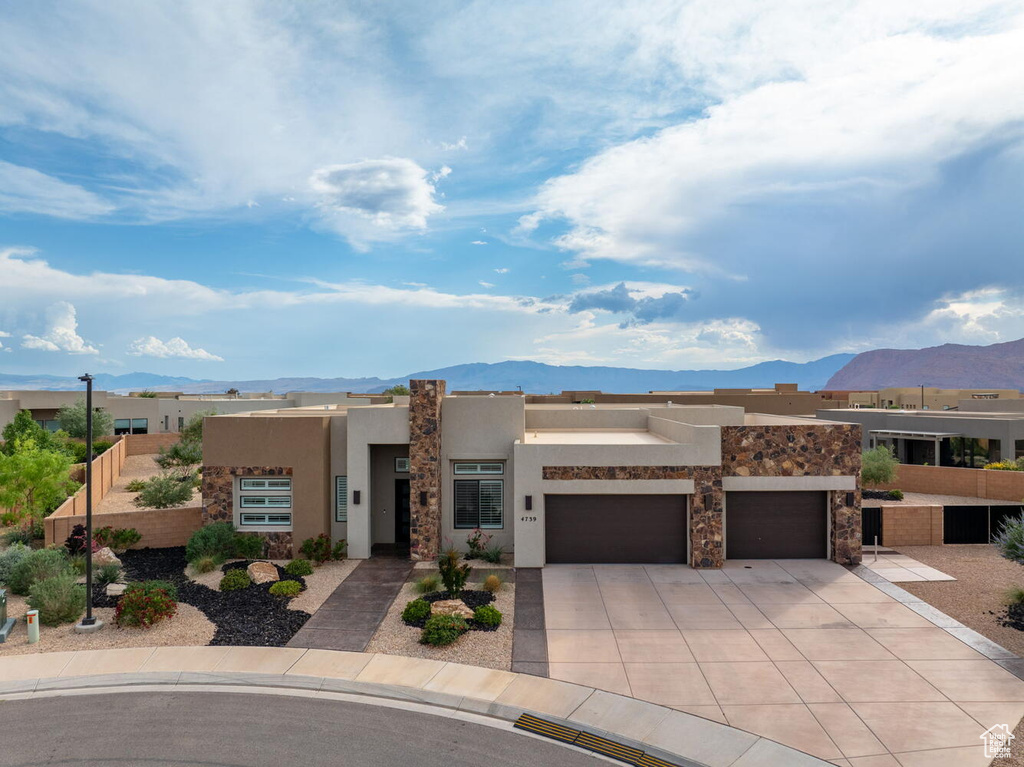 Pueblo-style house featuring a mountain view, stucco siding, concrete driveway, and an attached garage