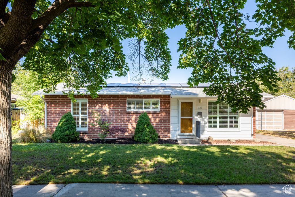 Ranch-style home with a front lawn, solar panels, brick siding, and entry steps