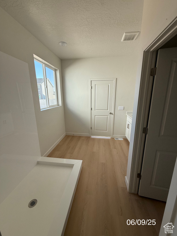 Hallway featuring light wood-type flooring, a textured ceiling, and baseboards