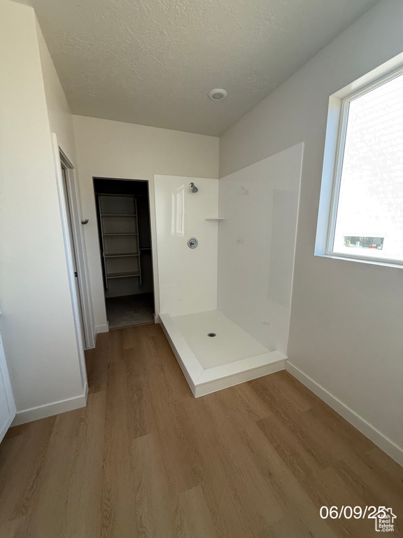 Full bath featuring a stall shower, wood finished floors, baseboards, and a textured ceiling