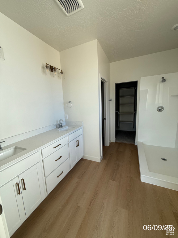 Bathroom with wood finished floors, a stall shower, a textured ceiling, and double vanity