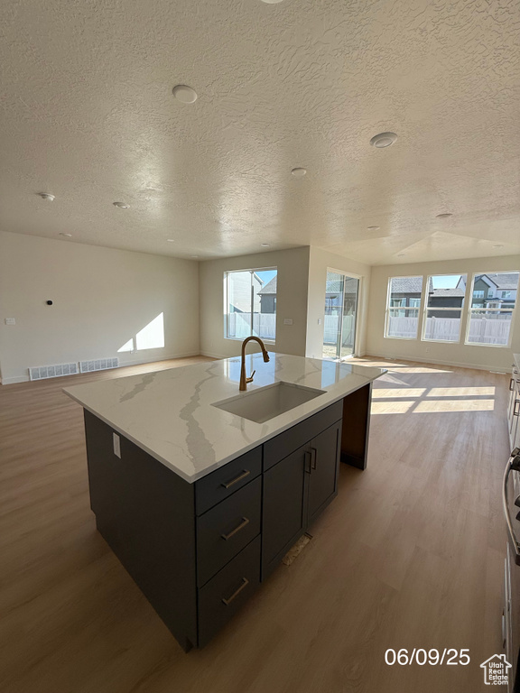 Kitchen featuring open floor plan, a sink, light wood-style floors, a textured ceiling, and a center island with sink