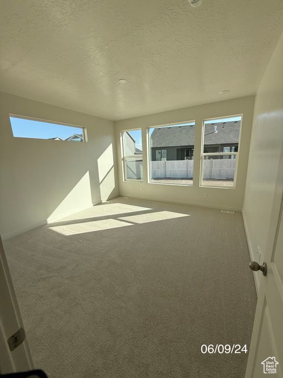 Spare room featuring carpet flooring, a textured ceiling, and baseboards