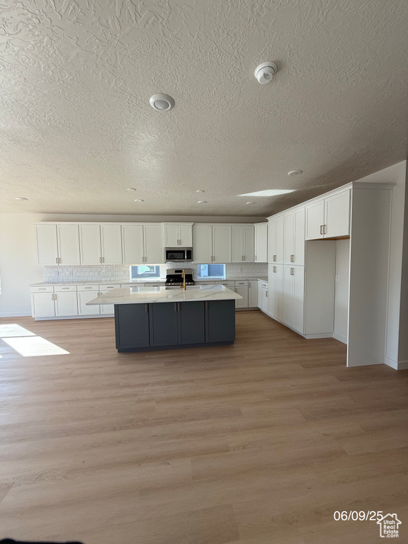 Kitchen featuring appliances with stainless steel finishes, white cabinets, a textured ceiling, light countertops, and light wood-style floors