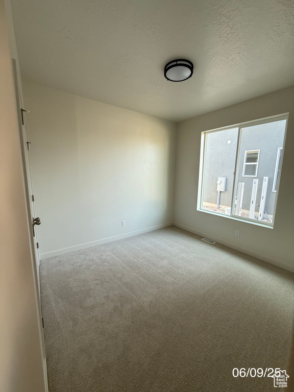 Spare room featuring carpet flooring, baseboards, and a textured ceiling