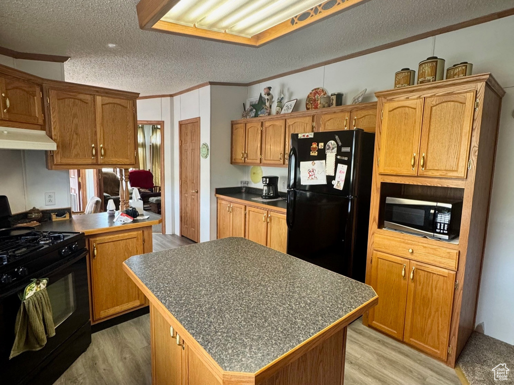 Kitchen with black appliances, a textured ceiling, a kitchen island, under cabinet range hood, and ornamental molding