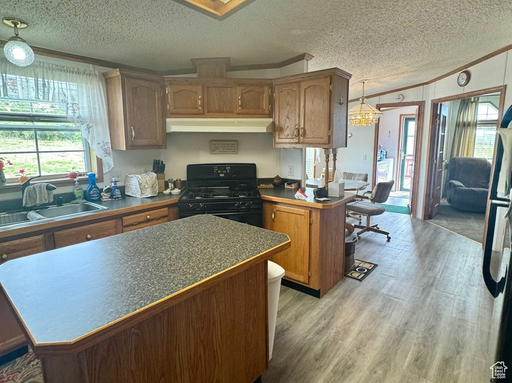 Kitchen featuring freestanding refrigerator, black gas stove, a textured ceiling, light wood finished floors, and a kitchen island