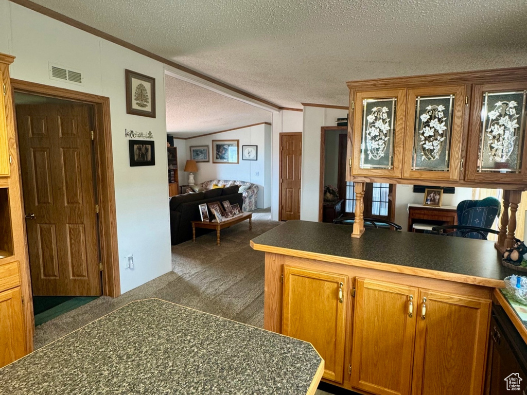 Kitchen featuring a peninsula, a textured ceiling, brown cabinetry, light wood-style floors, and ornamental molding