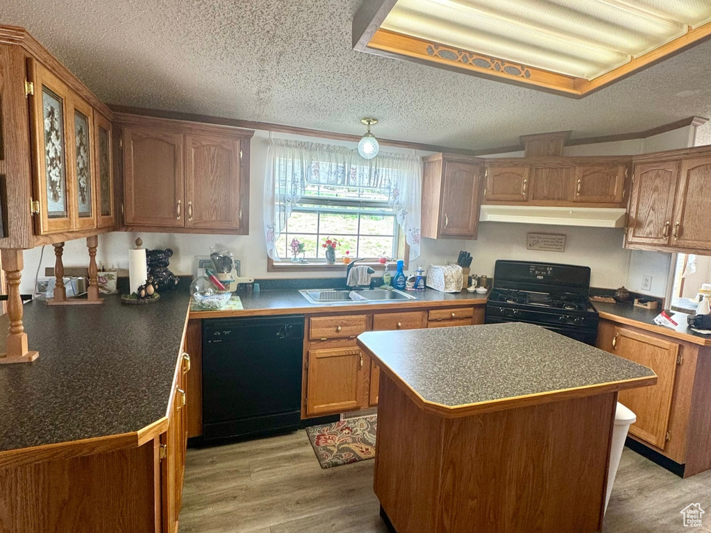 Kitchen featuring black appliances, a textured ceiling, light wood-style floors, under cabinet range hood, and a kitchen island