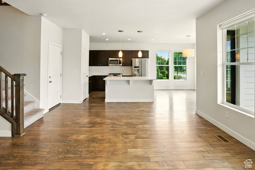 Kitchen featuring appliances with stainless steel finishes, light countertops, dark wood-style floors, an island with sink, and dark brown cabinets