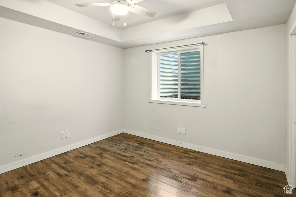 Unfurnished room with a tray ceiling, ceiling fan, and dark wood-style floors
