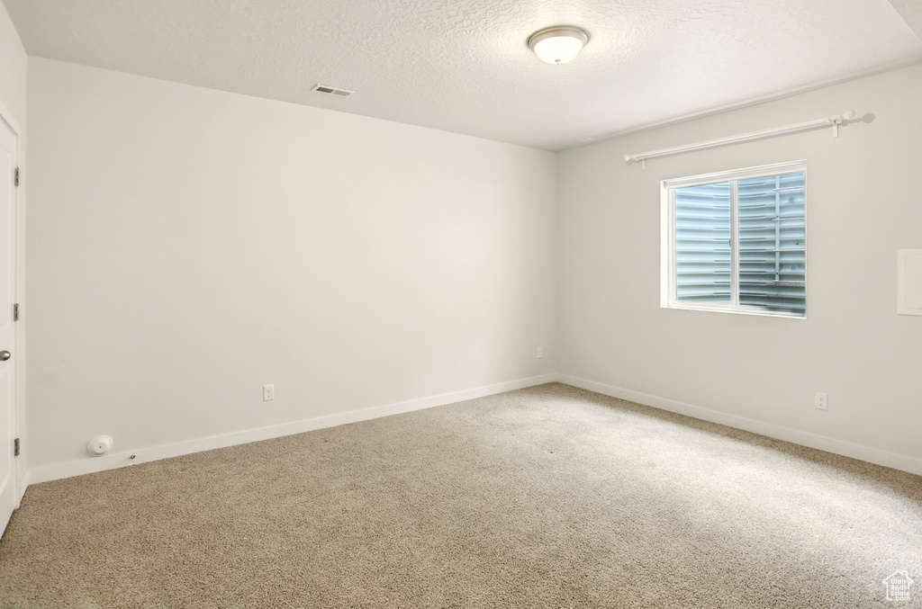 Carpeted spare room featuring a textured ceiling and baseboards